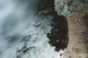 Aerial shot capturing reflections of clouds on water beside a tree-lined shore.