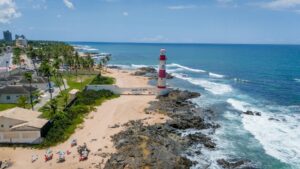 Aerial shot of Itapuã Lighthouse on a sunny beach in Salvador, Brazil, with waves crashing on the rocks.