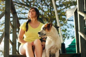 A cheerful woman sits with her dog on wooden steps, basking in the sun.
